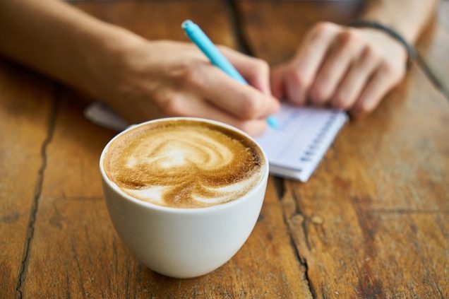 A person writing on a notebook next to a cup of coffee in the Montecristo Apartments in Stone Oak, TX.