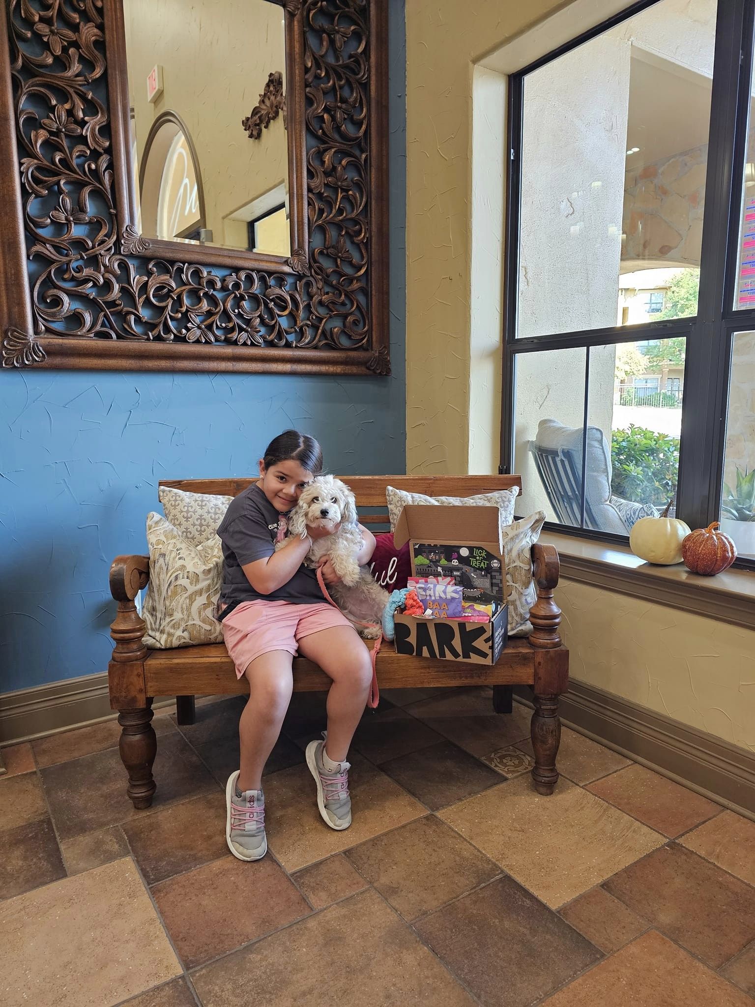 Apartments in Stone Oak San Antonio TX A child sits on a bench hugging a dog next to a ``Bark`` gift box, enjoying the cozy atmosphere. Decorative pillows, a large mirror, and pumpkins by the window create a warm setting for residents who appreciate comfort and convenience with quick service requests through Rent Online. The Montecristo Apartments in San Antonio North Loop San Antonio, TX 78232 p: (210) 672-4919 f: (210) 877-5455